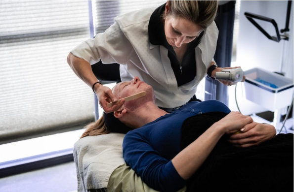 Woman in a chair as another woman administers warm wax to her neck and chin.