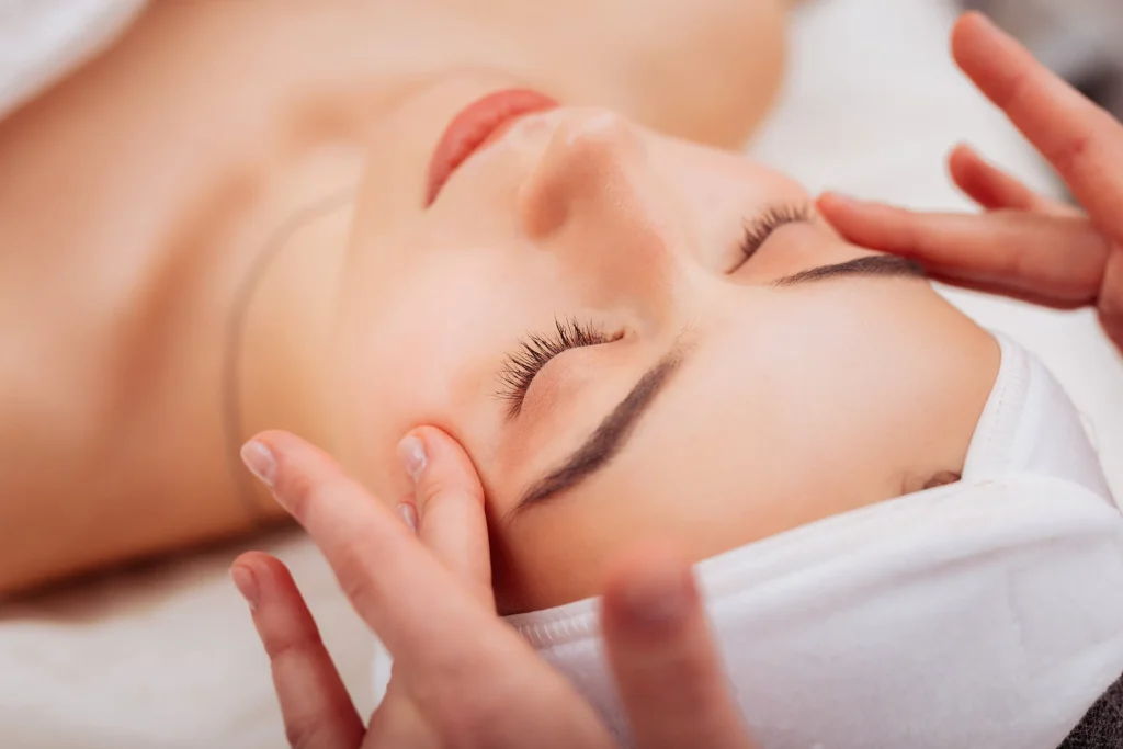 Relaxed woman's eyes closed while esthetician massages her temples