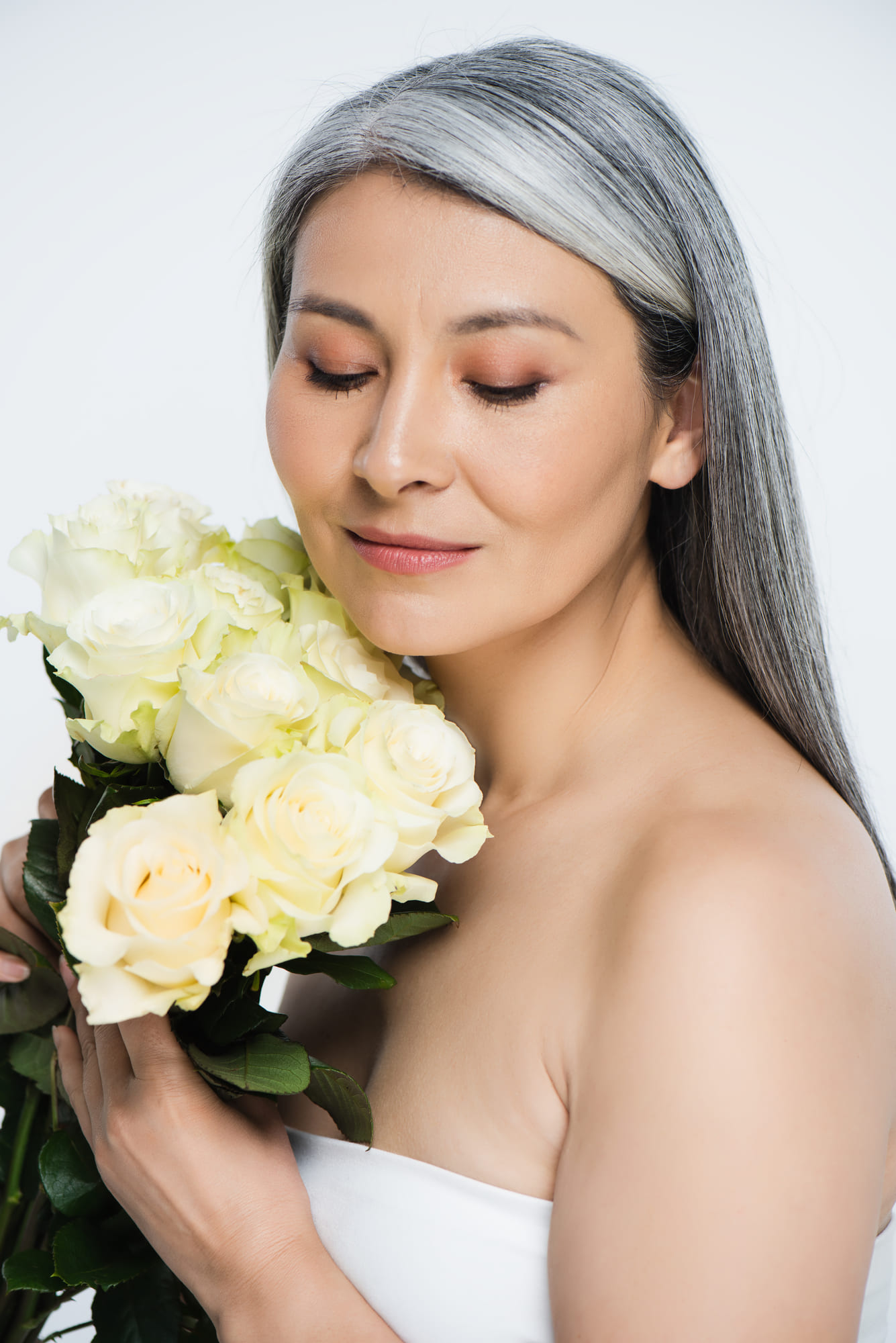A woman with gray hair holding a bouquet of pale yellow roses against a white background.
