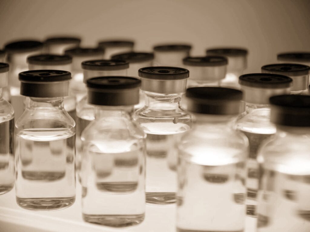 Rows of glass vials with dark stoppers, filled with liquid, in a warm sepia tone.