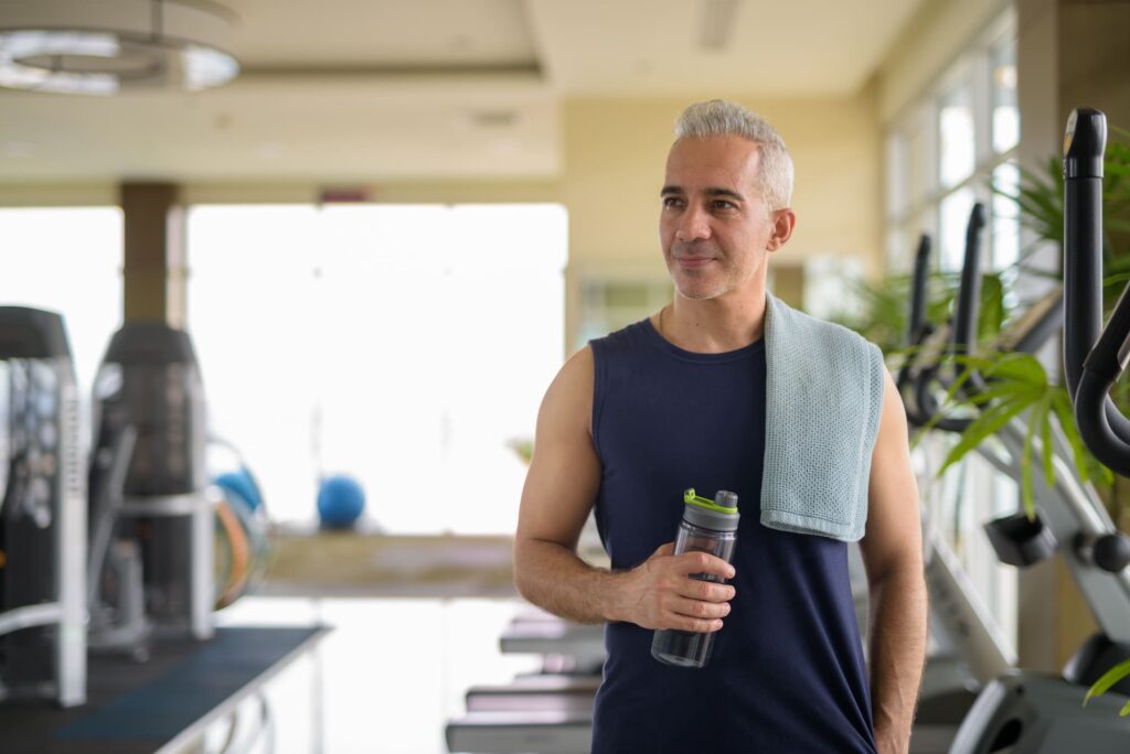 Man with gray hair holding a water bottle in a gym setting.