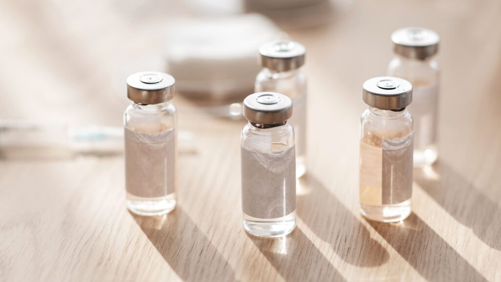 Five glass vials with metallic caps on a wooden surface.