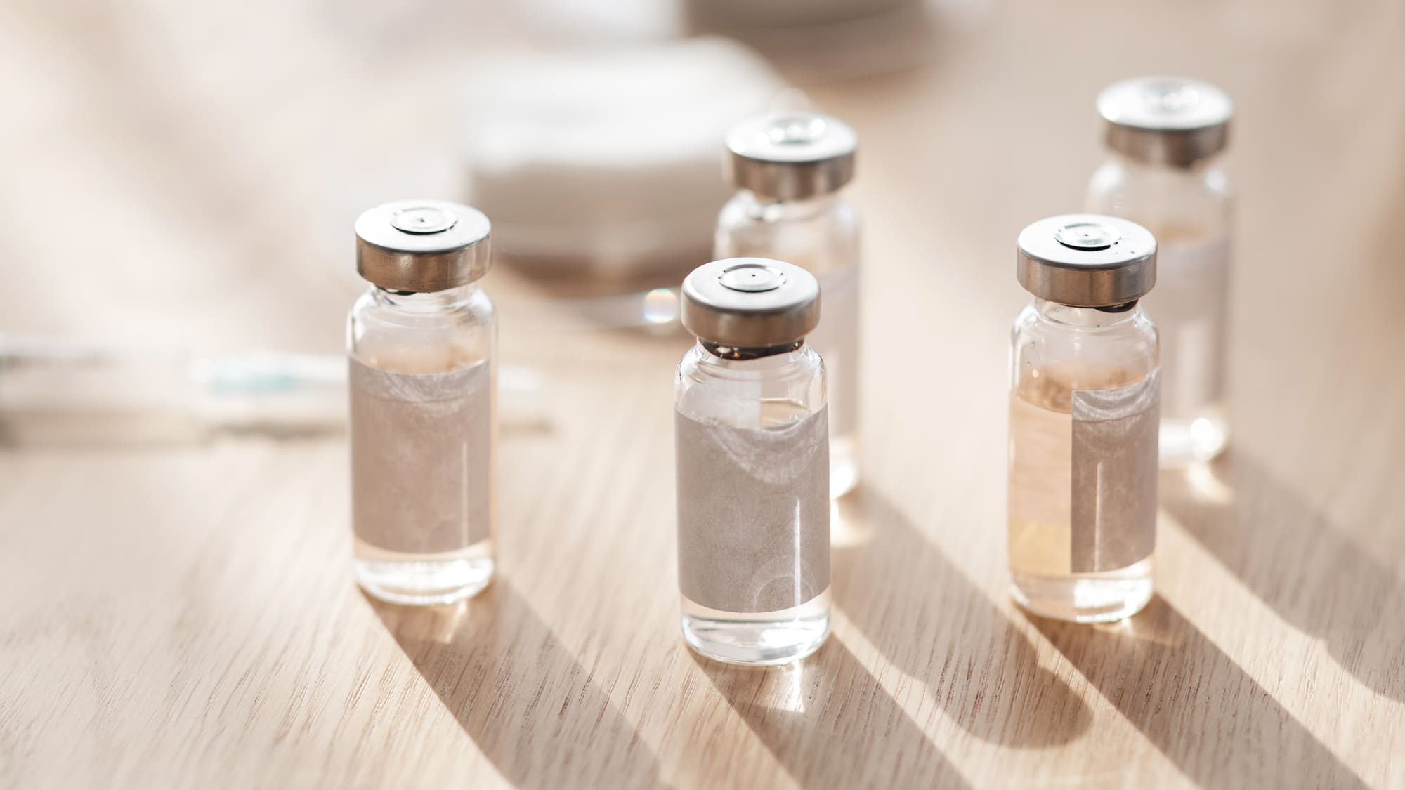Five glass vials with metallic caps on a wooden surface.