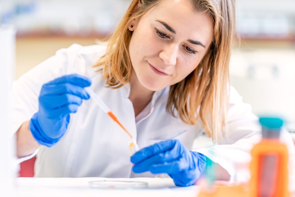 Person in a lab coat using a pipette in a laboratory.