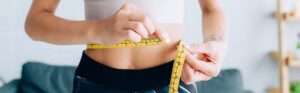 Woman measuring her wasteline after GLP-1 Medical Weight Loss